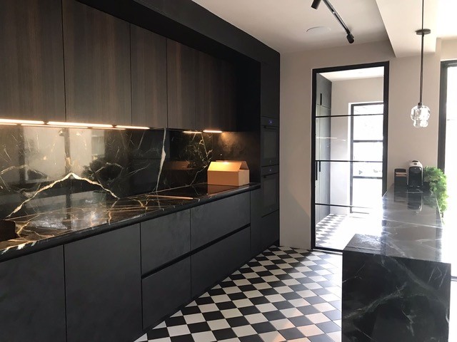 Discover where fire rated steel doors are commonly used 1 A modern black kitchen with marble backsplashes, featuring a single black-framed steel glass door leading to a checkered-tile utility area.